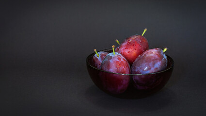 Fresh plum. Autumn harvest. Ripe purple plums in glass bowl on dark background. Concept: seasonal fruits, healthy food. Close up. Copy space for text.