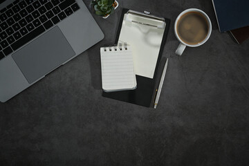Top view of modern workplace, laptop, notebooks, coffee cup and potted plant on black stone table