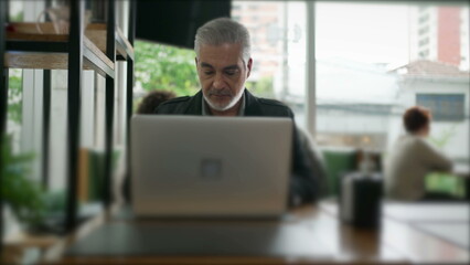 Male entrepreneur opening laptop at coffee shop table. Older middle aged person working remotely at cafe place using modern technology computer