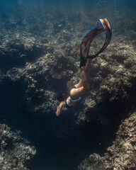 Female freediver fun diving descending into the crack in the reef in the ocean sea holding breath