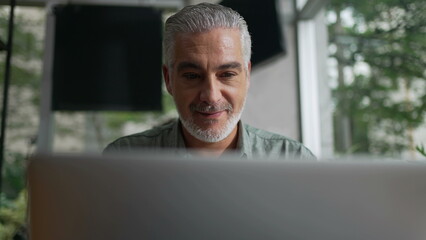 Fototapeta premium Happy older man using laptop computer at coffee shop. Closeup face of a senior entrepreneur looking at screen working remotely at cafe place
