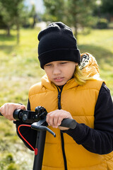 Naklejka premium Boy rides an electric scooter in autumn park. Schoolboy using e-scooter at sunny day.