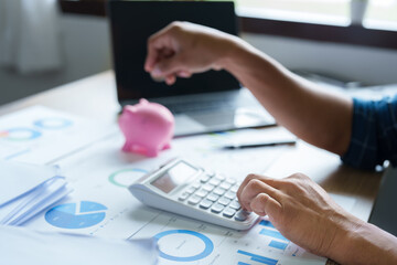 Portrait of an Asian businessman using a calculator to calculate his savings from SME operations, with a pink piggy bank as keep money concept