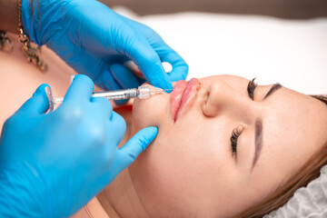 Obraz na płótnie Canvas Lip augmentation. Beautician injects hyaluronic acid into the lips of a girl with a syringe. The cosmetologist doctor performs the procedure in the cosmetology office. Plastic surgery.