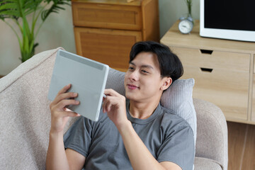 Portrait of an Asian teenager using a digital tablet on the sofa while relaxing at home