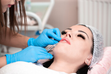 Lip augmentation. Beautician injects hyaluronic acid into the lips of a girl with a syringe. The...
