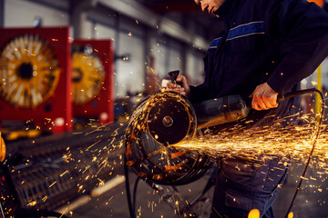 Cropped picture of a heavy industry worker who is grinding a metal framework with the grinding...