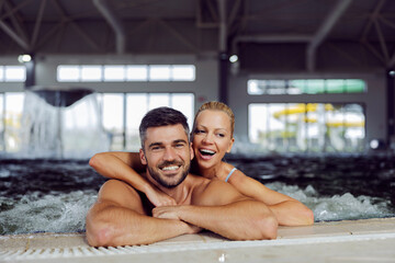 Couple hugging in the pool at spa center. A happy romantic couple in love standing in the pool with hot thermal and mineral water at the spa center and hugging.