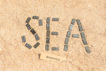 The word sea is laid out from dominoes on the sand. Sand inscriptions.