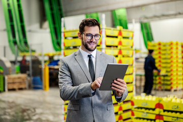 A business owner monitoring works in fruit production factory warehouse over the tablet and smiling...