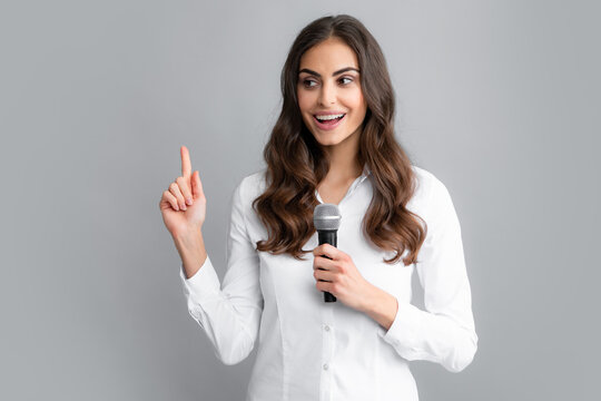 Woman speech, business woman holding a microphone. Young woman talking in microphone, perfom with mic, giving speech, standing on gray background.