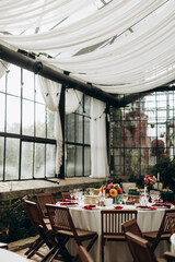 a decorated party hall with many windows and white capes. numbered and decorated tables with transparent glasses, white dishes and red napkins. 