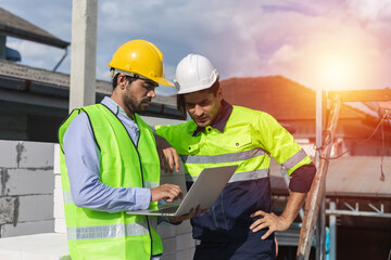 Professional construction engineer team, Two man engineer wear uniform holding laptop standing at construction site. Workers supervise the construction of the building.