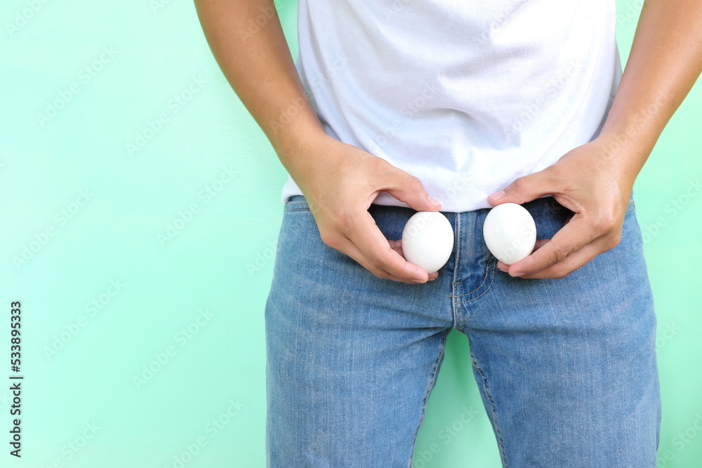 Wall mural men reproductive and male testicle health concept. young asian man holding two chicken eggs on crotc