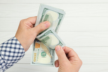 Two hands of a woman with a stack of one hundred dollar bills on the background of light wooden boards. Person counts cash dollars.