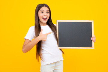 Fototapeta na wymiar Teenager younf school girl holding school empty blackboard isolated on yellow background. Portrait of a teen female student. Excited teenager, glad amazed and overjoyed emotions.