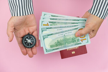 Human hands holds manual travel compass and cash dollars over a biometric passport on a pink background. Vacation planning concept, travel, open borders.