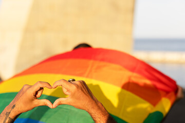 Hands making heart sign in front of rainbow flag