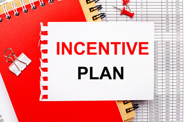 Against the background of the reports, there are red and brown notepads, a white paper clip, red buttons and a white sheet of paper with the text INCENTIVE PLAN. Business concept