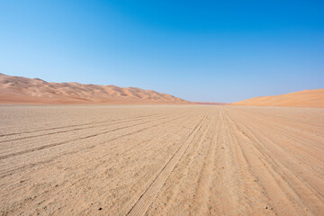 Fototapeta na wymiar Track in the desert going thru a sabkha with blue sky and copy space. Middle East, Arabian Peninsula 