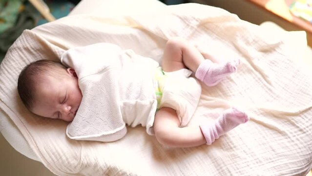 baby girl newborn sleep in a straitjacket. cute infant lying on the bed legs in socks close-up. happy family kid dream concept. baby newborn dark brunette close up lifestyle