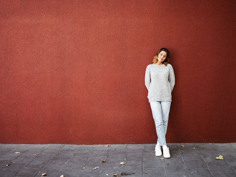 Woman stands in front of a red wall and relaxes with closed eyes, copy space