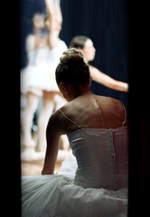 A ballerina backstage of a performance at a theatre on stage. Ballet dancer sitting on the floor while play or concert is happening. She is getting ready, doing warm up and preparing to dance