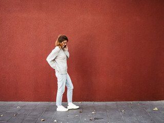 Woman stands talking on phone in front of red wall and looks down, copy space