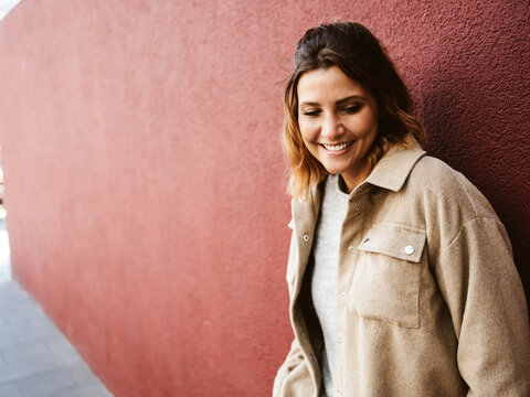 Woman standing in front of red wall looking down laughing, copy space