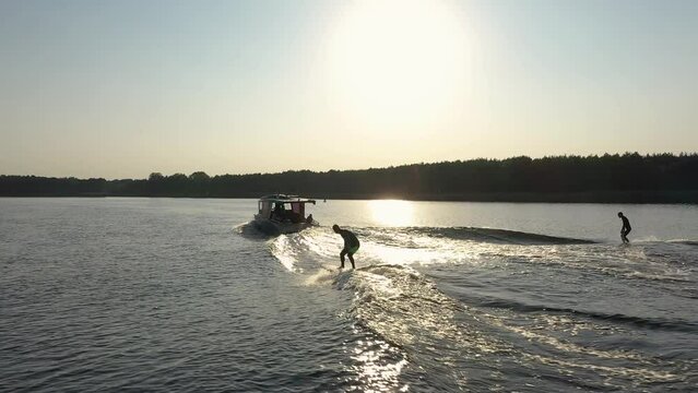 two surfers on surfboard surfing waves behind boat in sunset 005
