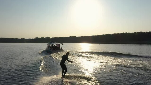 surfer on surfboard surfing waves behind boat in sunset 003