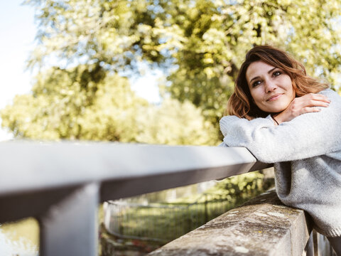 Young woman leans on wooden railing in park and looks dreamily to the side