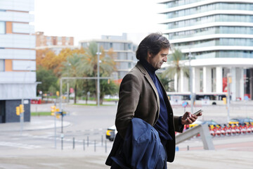 Confident man looking to mobile phone while walking on a street, man in suite walking on a street wall with copy space