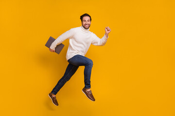 Fototapeta na wymiar Photo of energetic active programmer guy jump run carry pc device wear white sweater jeans isolated yellow color background