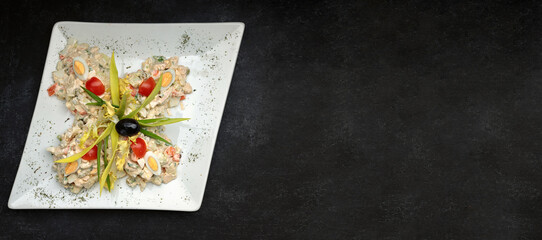 Olivier salad on a white plate on a dark background