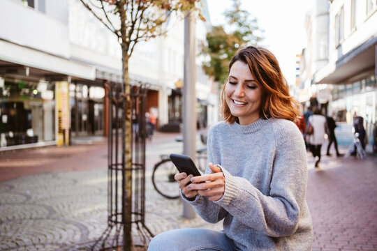 Young woman looking at her smartphone downtown laughing
