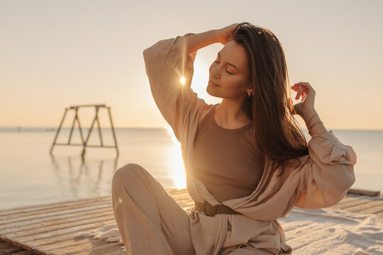 Summer lifestyle, young caucasian brunette with straight hair on beach. Girl closing her eyes enjoying sun at dawn by sea. Rest and recovery concept.