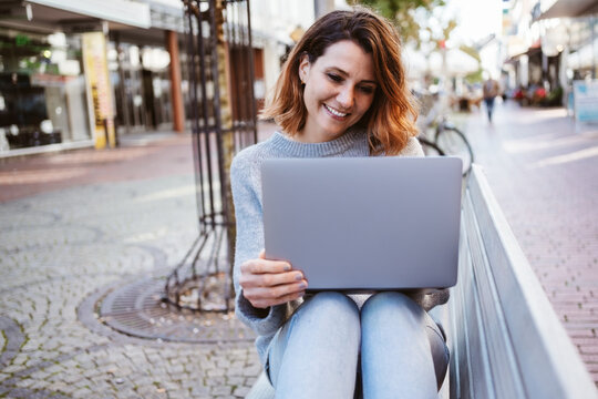 Laughing young woman with laptop sitting on a park bench downtown