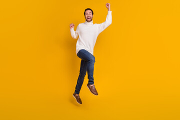 Fototapeta na wymiar Photo of lucky pretty guy wear white pullover jumping high rising fists isolated yellow color background