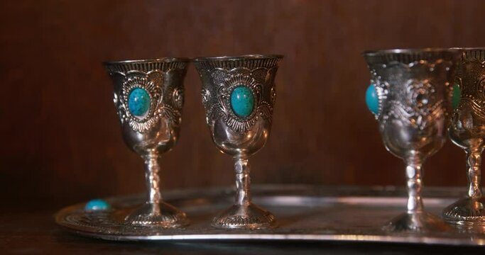 Antique silverware trembles from earthquake close-up. Tray of silver shot glasses and turquoise gem shakes from sea in cruise bar. Shaking earthquake in museum collection of precious silverware.