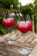 red cocktail with ice in glass with stem on wooden surface