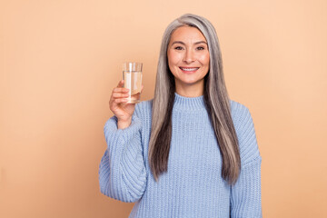Photo of cute adorable retired woman wear blue sweater holding glass water isolated beige color background