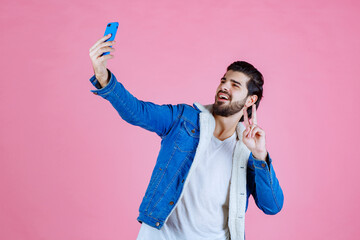 Young man taking a selfie against a pink background, dressed in a blue jacket and white shirt, capturing a casual and vibrant moment