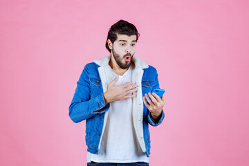 Young man using smartphone while standing against a pink background, casual fashion style, focused on technology and communication.