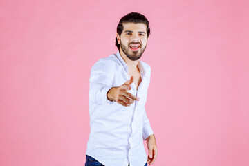 Young man in white shirt making a peace sign gesture against a pink background