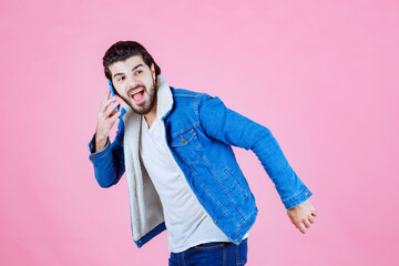 Young man in casual attire holding a smartphone against a pink background, expressing excitement or surprise with a dynamic pose and energetic stance.