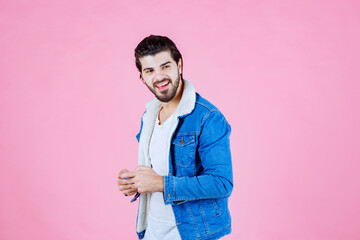Young man in a bright blue denim jacket and white shirt standing against a solid pink background, casual pose, modern fashion style, vibrant colors, fashion photography