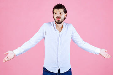 Person with open arms standing against a pink background, expressing openness and friendliness, dressed in a white shirt and dark pants, conveying a welcoming and positive attitude.