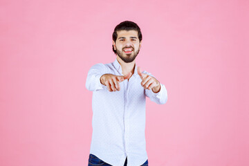 A person with a blurred face stands against a pink background, wearing a white shirt and holding a string or object in their hands, creating a playful or casual scene.