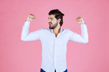 Confident person with flexed arms wearing a white shirt against a pink background